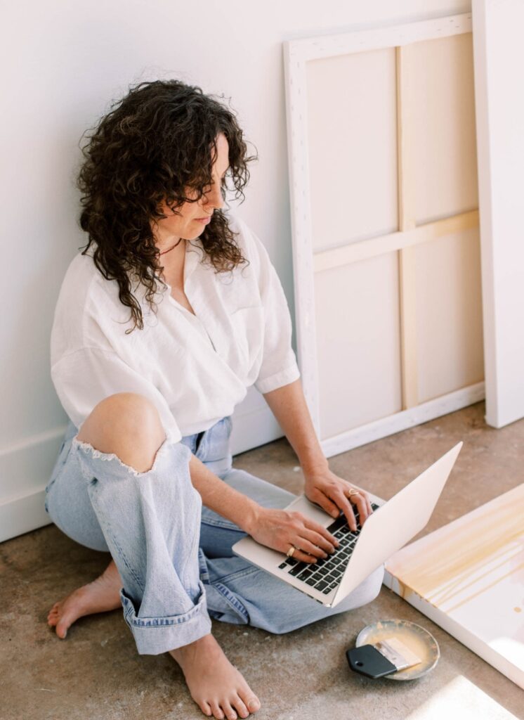 A woman seated on the floor, focused on her laptop, illustrating a creative workspace for a blog on tidying up in Canva.